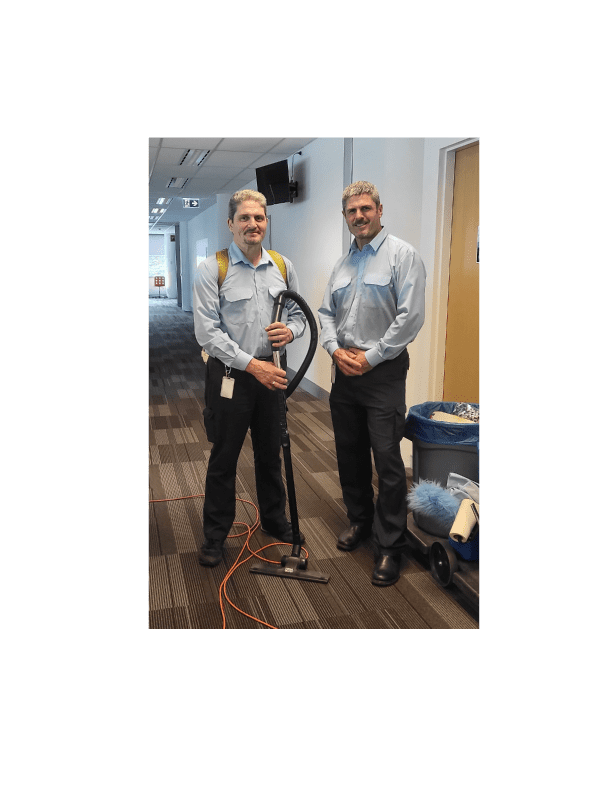 Grant and Craig from Cleanzone posing in uniform with cleaning equipment in a Canberra office